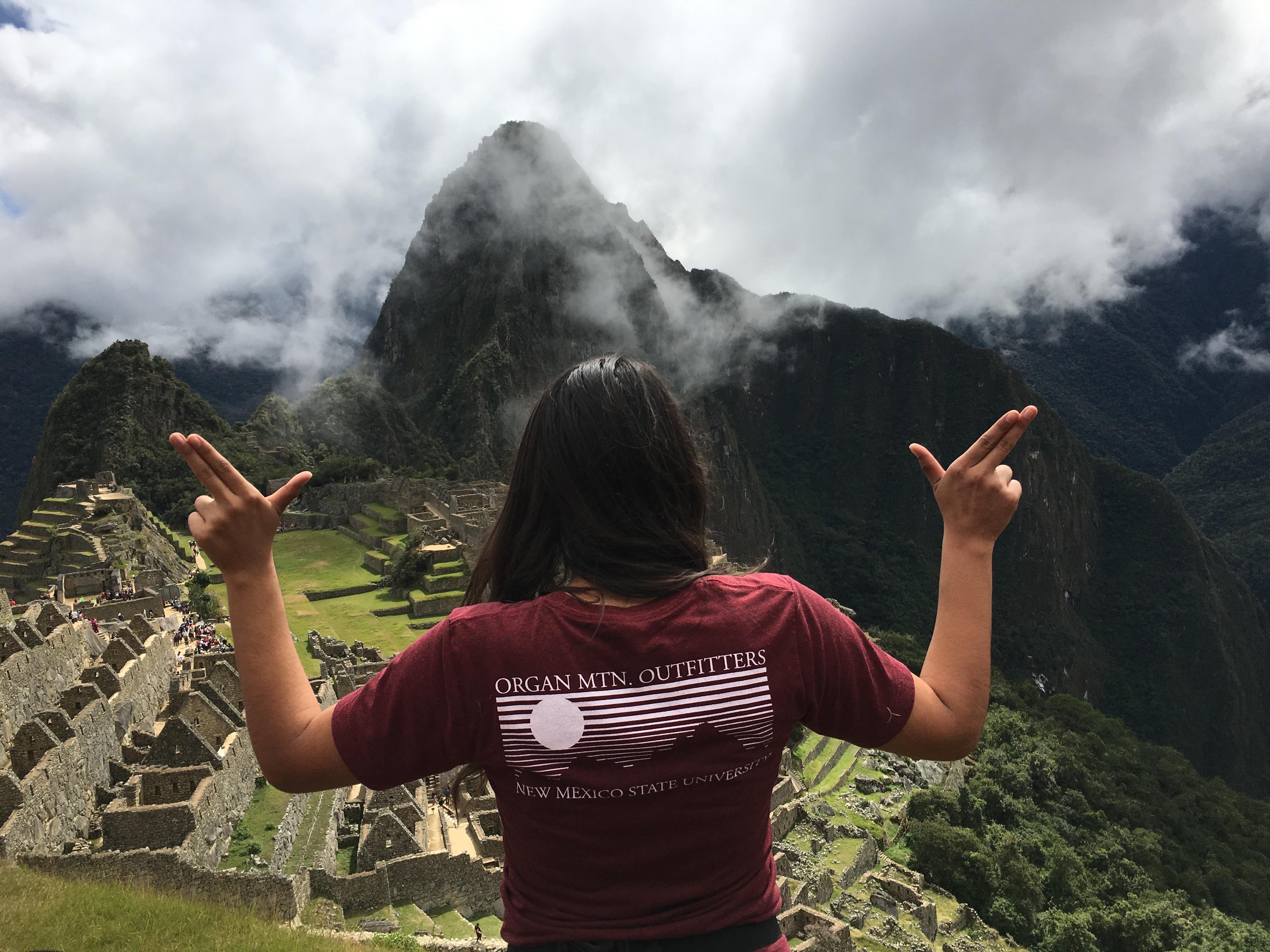 Student poses with her back to the camera in front of Machu Picchu in the "Aggies Up" pose